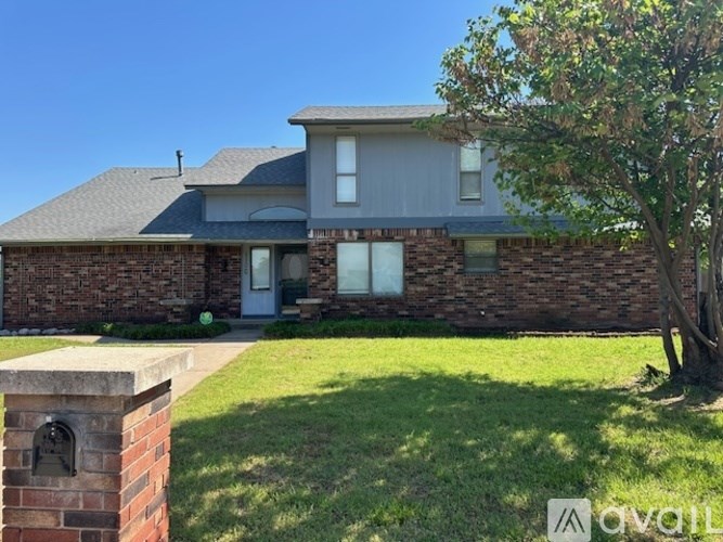 A house with a grey roof and a brick wall with a tree in front.