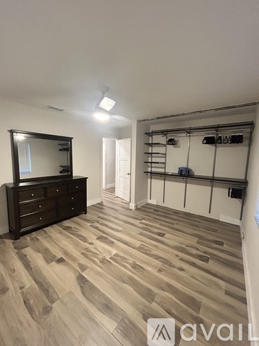 A room with wooden flooring and a black dresser with a mirror.