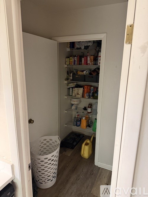 A white door is open to a small pantry with shelves full of food and drinks.