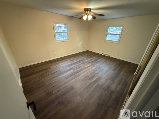 A room with wooden flooring and two windows.