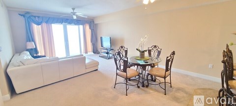 A living room with a white couch, a television, a dining table with chairs, and a window with curtains.