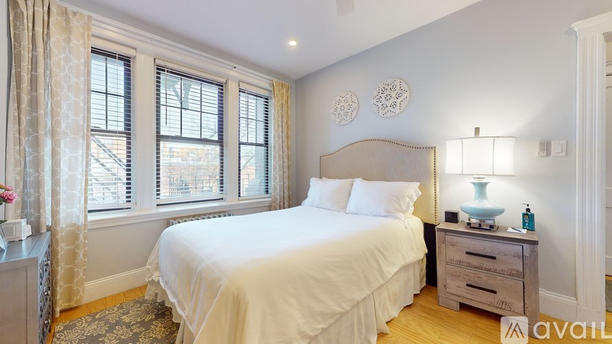 A bedroom with a large bed, a nightstand with a lamp, and a window with curtains.