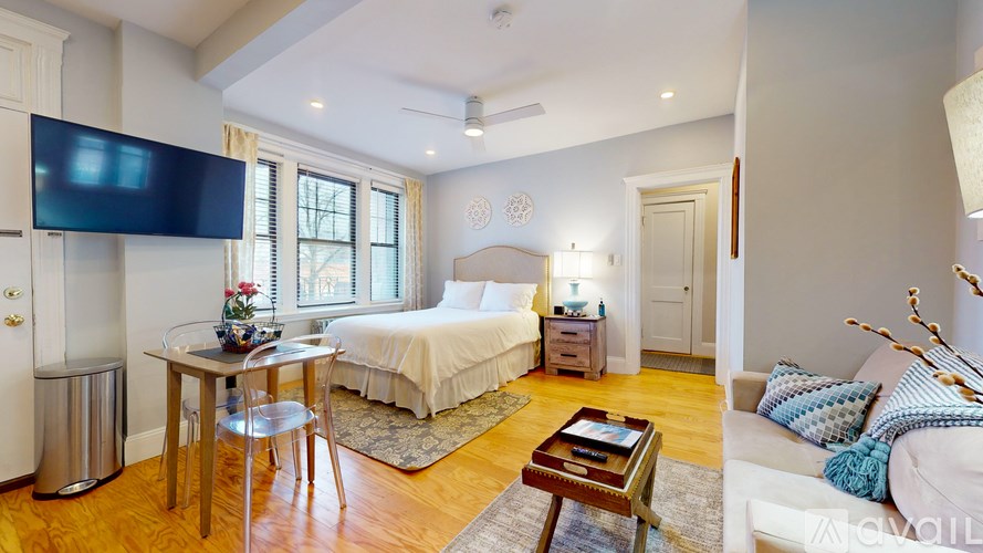 A bedroom with a bed, a couch, a table, and a TV mounted on the wall.