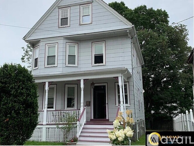 A white house with a front porch and a flower pot on the steps.