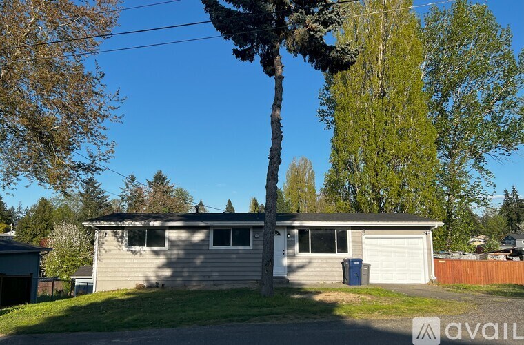 A house with a grey roof and a white garage door is surrounded by trees.