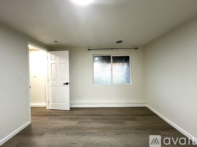A room with a door and a window with a white wall and wooden floor.