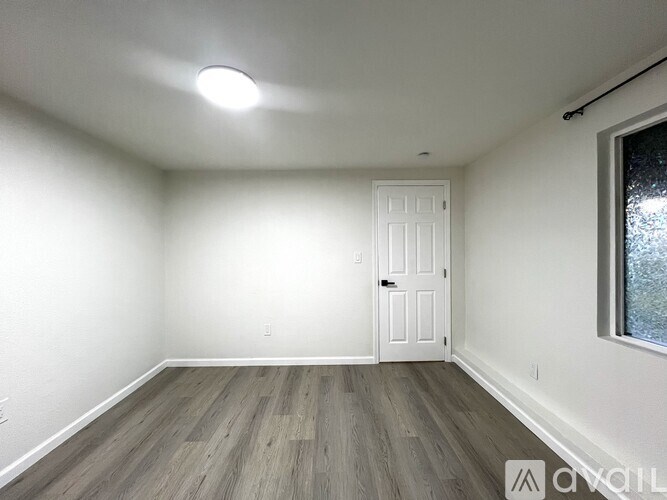 A room with a white door and a window with a view of trees outside.