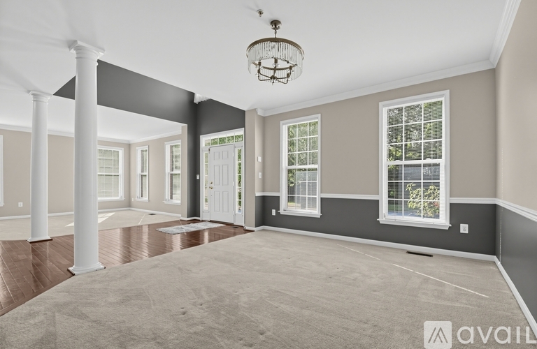 A spacious room with a carpeted floor, a chandelier, and a door with a window above it.