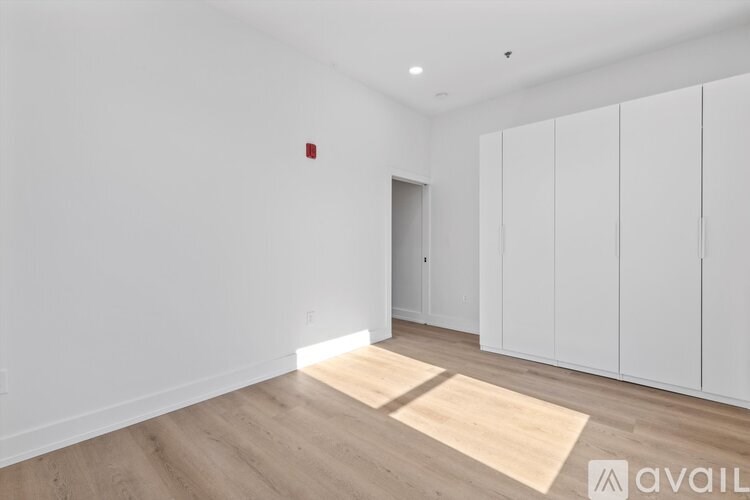A room with white walls and wooden flooring, with a small red object on the wall.