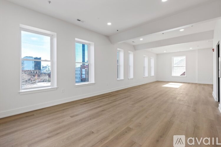 A spacious room with wooden floors and large windows overlooking a cityscape.