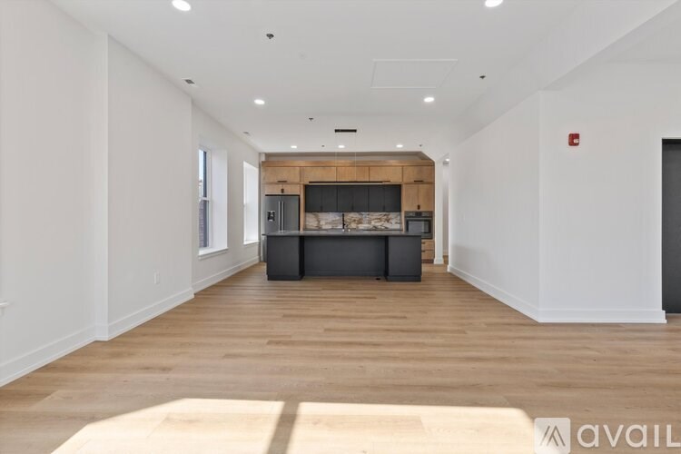 A spacious room with wooden flooring and a kitchen area in the background.