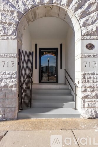 A white stone archway with a black gate and a number 713 on the wall.