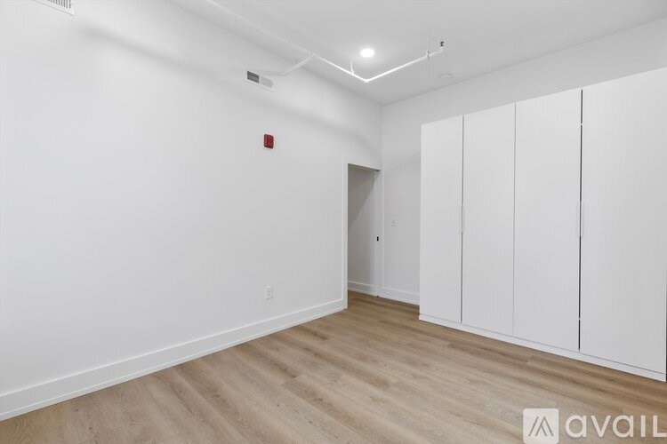 A room with white walls and wooden flooring, with a red object on the wall and a white door.