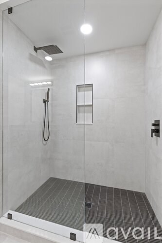 A shower area with a glass door and a black mat on the floor.