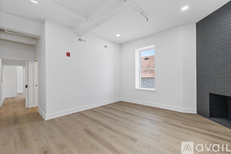 A spacious room with wooden flooring and a fireplace on the right side.