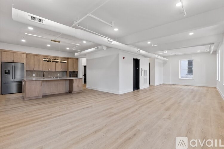 A spacious room with wooden flooring and a kitchen area with brown cabinets and a stainless steel refrigerator.