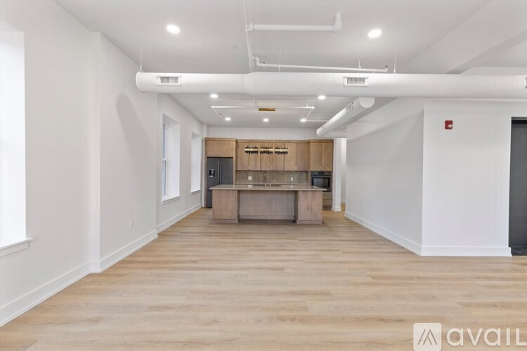 A spacious room with wooden flooring and a kitchenette in the background.