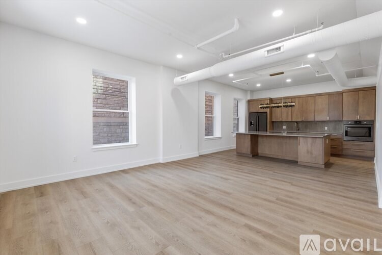 A spacious room with wooden flooring and a kitchen area in the background.