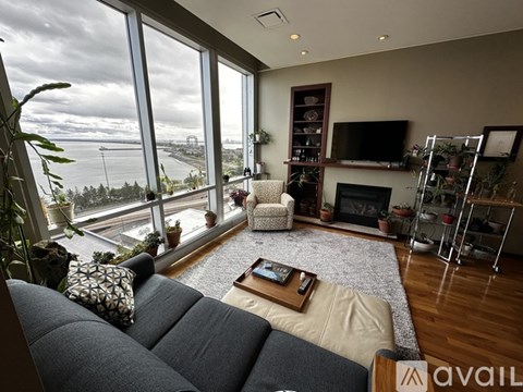 A living room with a grey couch and a large window overlooking the water.