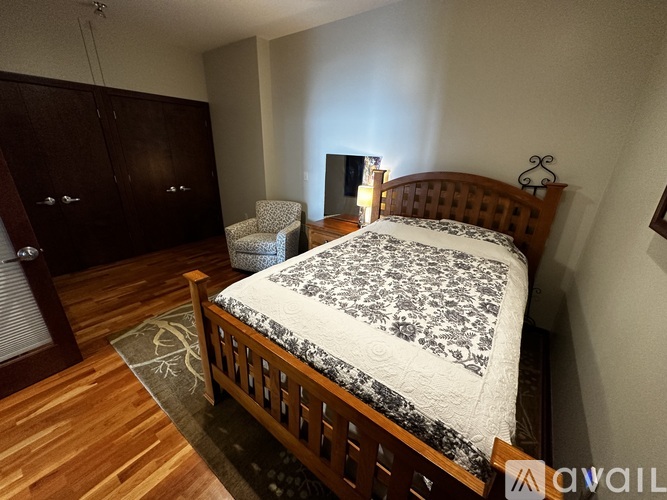 A bedroom with a bed, chair, and wooden floors.
