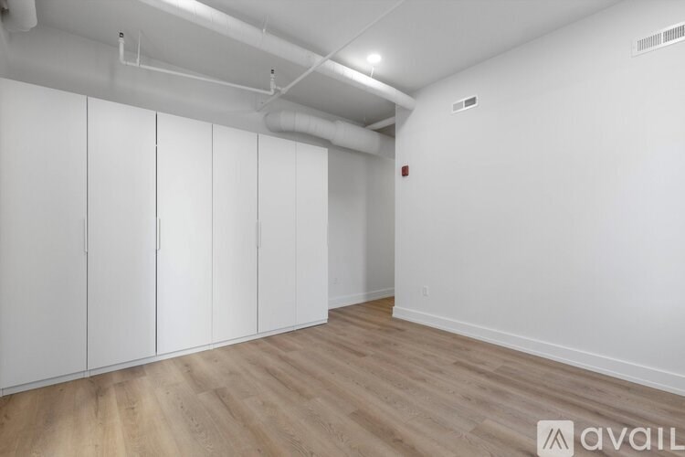 A room with white walls and wooden flooring, featuring a row of white cupboards.