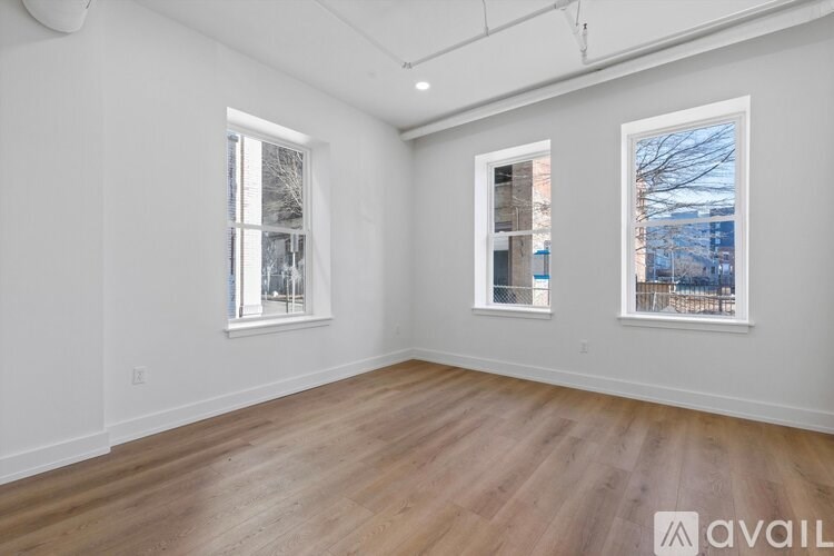 A spacious room with wooden floors and two windows.