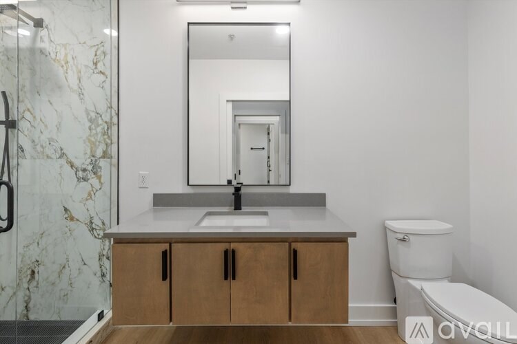 A bathroom with a marble shower, wooden vanity, and a toilet.