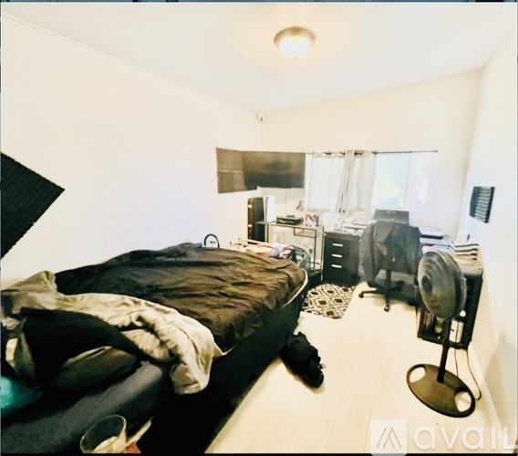 A bedroom with a bed, a desk with a computer, and a fan.