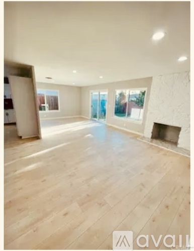 A spacious room with wooden flooring and a fireplace.