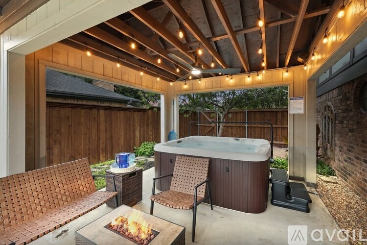 A hot tub is surrounded by chairs and a table with a fire pit in the middle of a backyard.