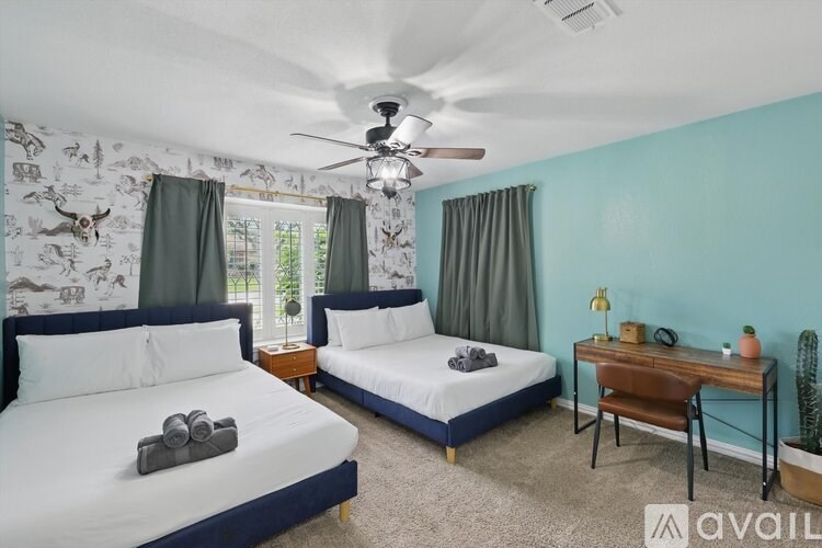 A bedroom with two beds, one of which has a towel on it, and a desk with a chair.