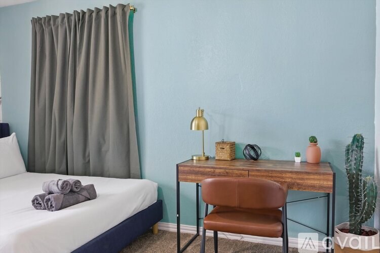 A bedroom with a bed, desk, chair, and a cactus.