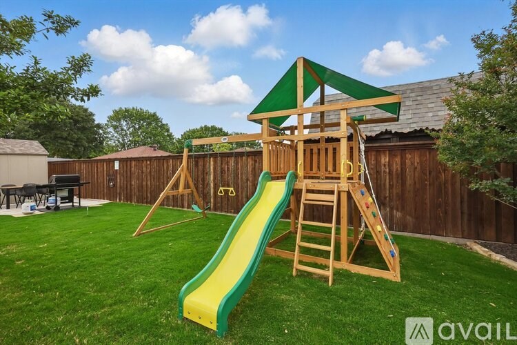 A wooden playset with a green slide in a backyard.