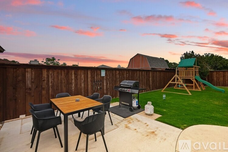 A backyard with a wooden fence, a table with chairs, a grill, and a slide.