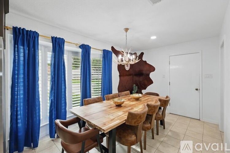 A dining room with a wooden table and chairs, a chandelier, and blue curtains.