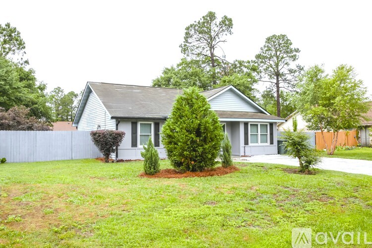 A house with a grey roof and a white fence is surrounded by greenery.