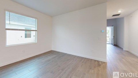 A spacious room with wooden flooring and a window with blinds.