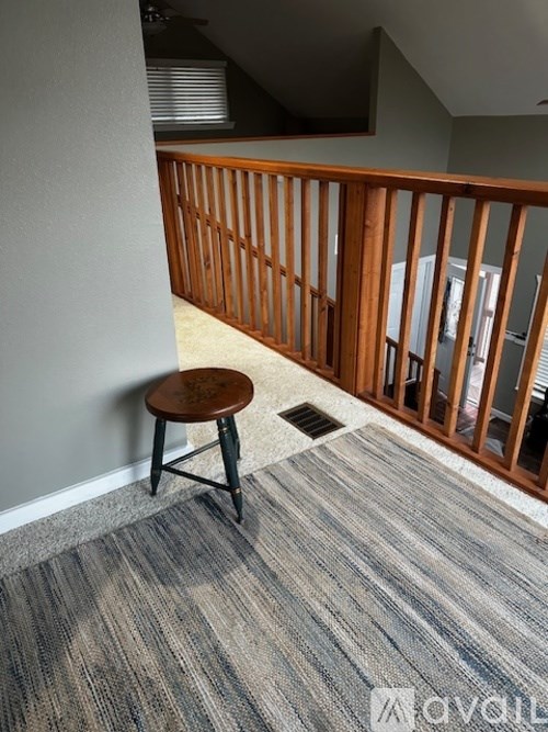 A room with a grey carpet and a wooden stool.