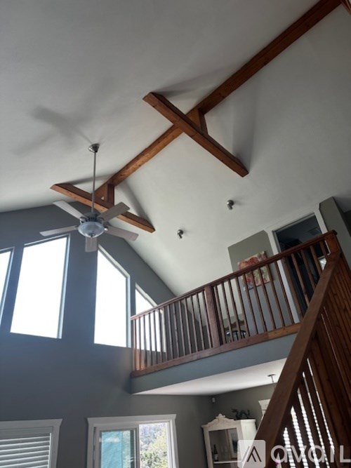 A ceiling fan hangs from a wooden beam in a room with a balcony.