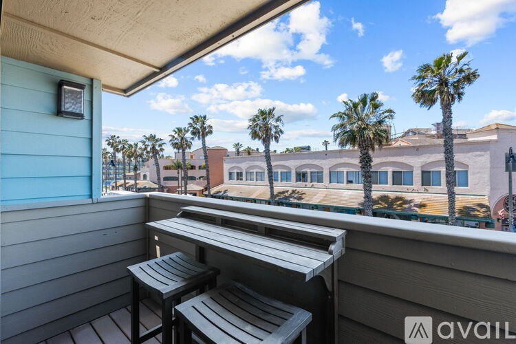 A balcony with a table and two chairs overlooks a building and palm trees.