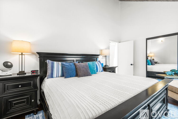 A bedroom with a large bed, a nightstand with a lamp, and a mirror on the wall.