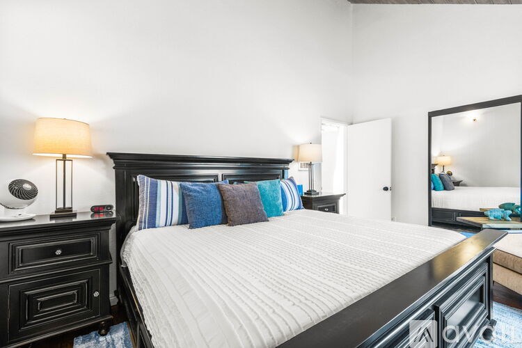 A bedroom with a large bed, a nightstand with a lamp, and a mirror on the wall.