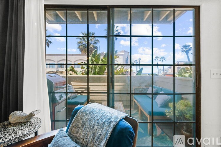 A chair with a blue blanket is in front of a window with a view of a pool and palm trees.