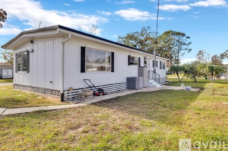 A mobile home with a white exterior and a black roof is surrounded by a grassy area and trees.