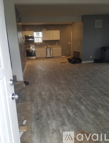 A room with a kitchen in the background and a hallway leading to a door.