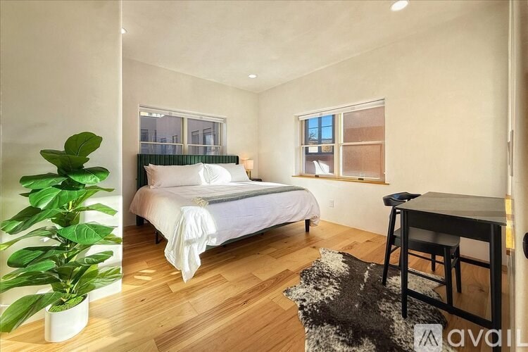 A bedroom with a large bed, a desk, and a potted plant.