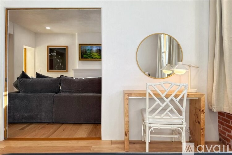 A white chair sits in front of a round mirror on a wooden table.