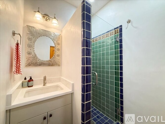 A bathroom with a white sink and a blue tiled shower.