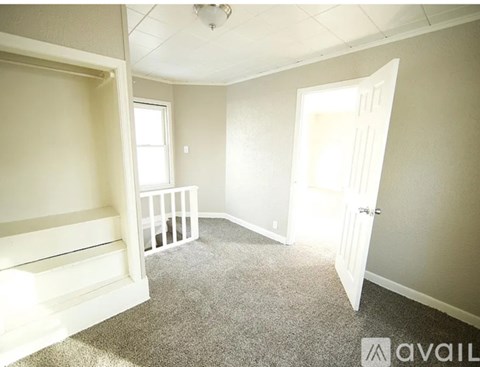 A room with a carpeted floor, a door, a window, and a staircase.