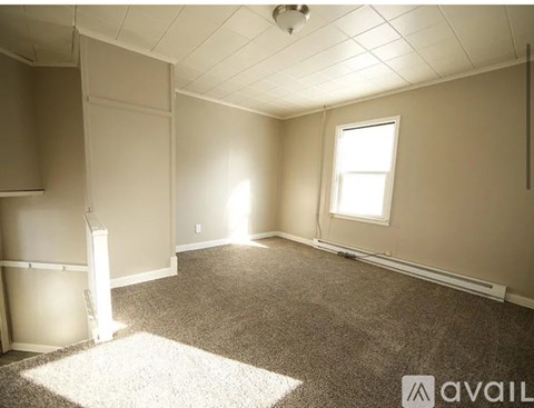A room with a carpeted floor, a window, and a ceiling with a grid pattern.